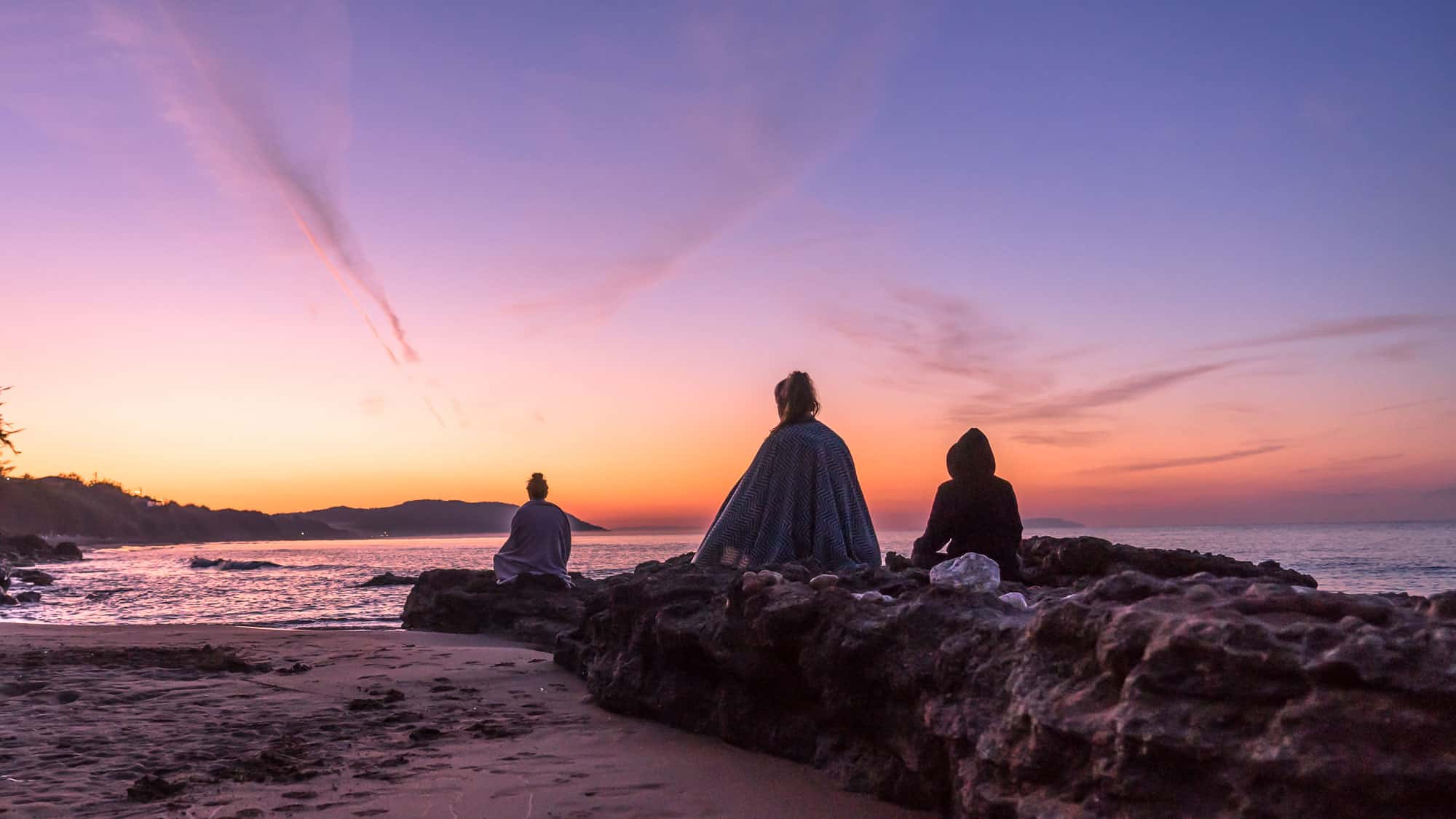 Yoga students meditating on the beach as the sun rises across the water during their yoga training