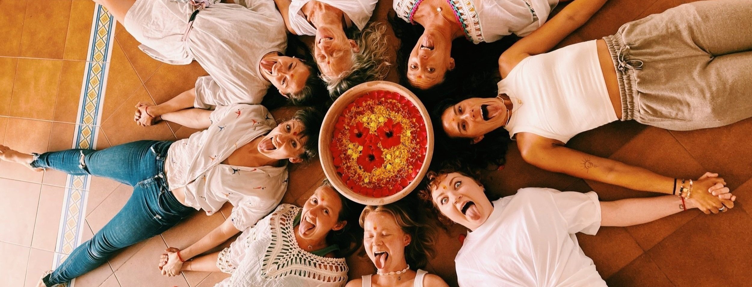 Yoga teacher training students in a fun pose lying down and holding hands