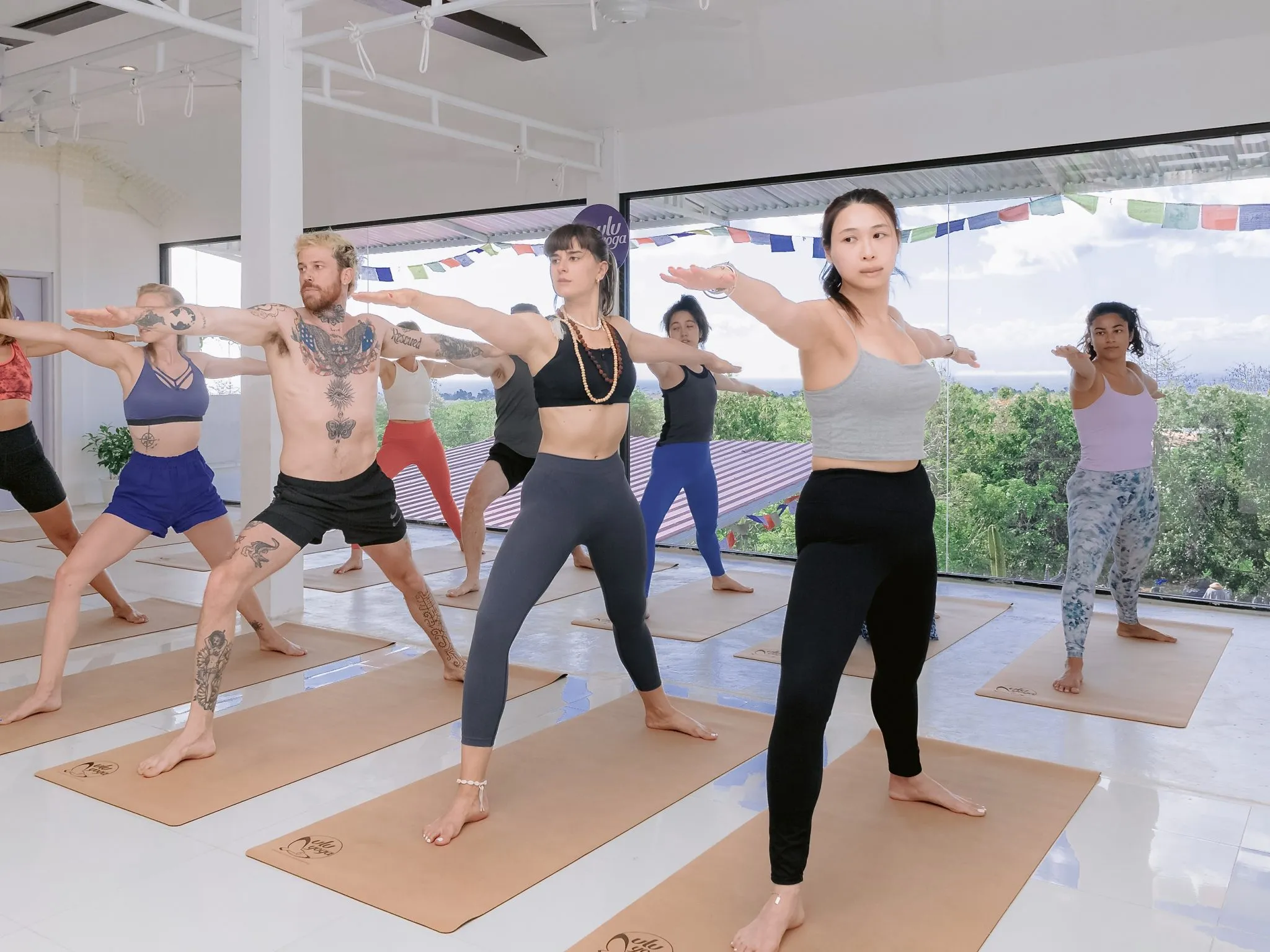 Yoga students in warrior two position in the studio during asana class as they practice for their yoga teacher training certification in Bali.